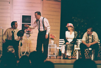 An older standing man talking with a younger sitting man with an man and a woman looking on 
