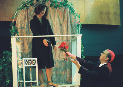 A man handing flowers up to a woman on a balcony