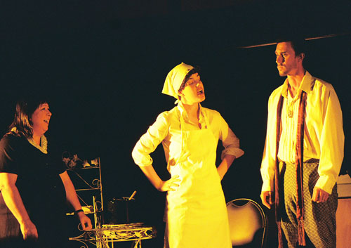 A woman wearing an apron talking to a man with a goatee with another woman looking on 