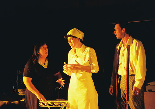 A woman wearing an apron talking to another woman with a man in a goatee looking on 