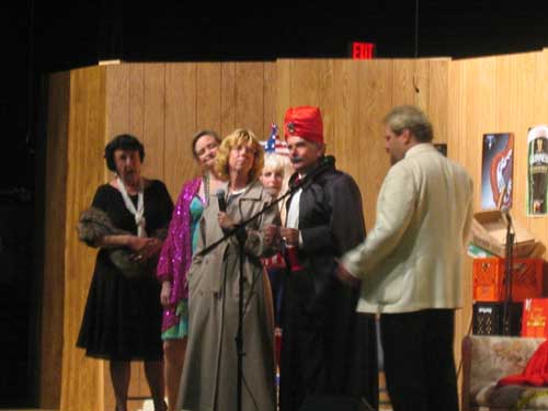A woman in a black dress and mink stole, a woman in a sparkling purple coat, a blond woman, a woman in a brown raincoat, a man in a suit,
       black cloak and red turban, and a man in a white tuxedo jacket