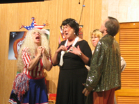 A woman in a red, white and blue outfit, a woman in a black dress and stole, and a man in a sparkling gold shirt, all crying