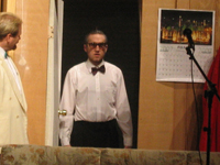 A man wearing a tuxedo shirt, bowtie and glasses standing in the doorway