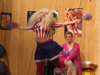 A woman in a red, white and blue outfit dancing while a woman in a sparkling purple coat sits behind her