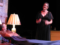 A woman standing talking to a man reclining in bed