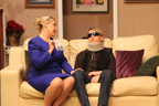 A woman in a blue skirt sitting on a couch talking to a man wearing a neckbrace and sunglasses
