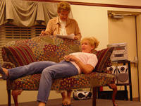 A woman standing over another woman reclining on a couch