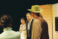 A man in a suit addresses a man in a cowboy hat while two women look on