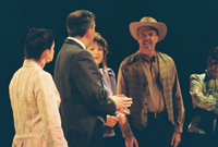 A man in a cowboy hat talks to a man in a suit while three women look on