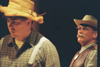 A young man in a hat in the foreground and an older man in a cowboy hat in the background