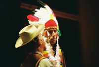 A man in a cowboy hat talking to a Native American man in a headdress