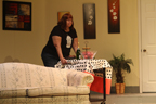 A woman wheels a table with a bottle and a bowl into a living room