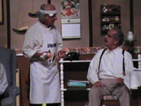 A man with a bandaged head speaking with a seated man with glasses and a moustache